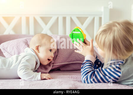 Two cute little siblings playing together on bed. Sister and brother having fun at bedroom in morning. Happy family with children Stock Photo