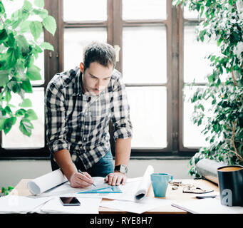 Young man architect working on architectural project in design studio. Modern office concept with green plants. Stock Photo