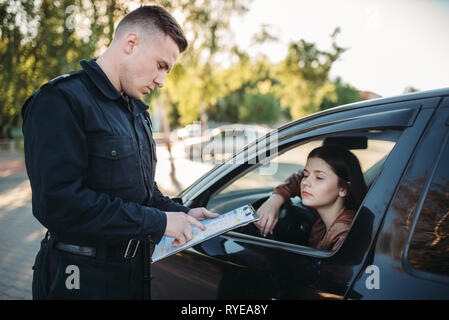 Policeman in uniform writes fine to female driver Stock Photo