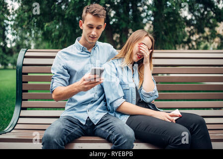 Phone addicted people, couple on the bench in park Stock Photo