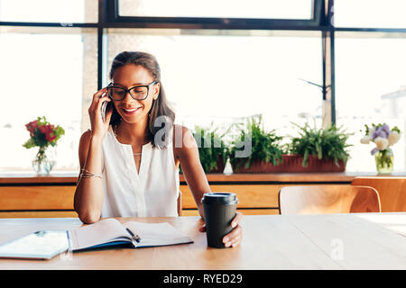 Smiling female entrepreneur talking on smartphone in cafe Stock Photo
