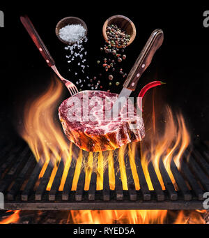 Raw Steak ribeye cooking. Conceptual picture. Steak with spices and cutlery under burning grill grate. Stock Photo