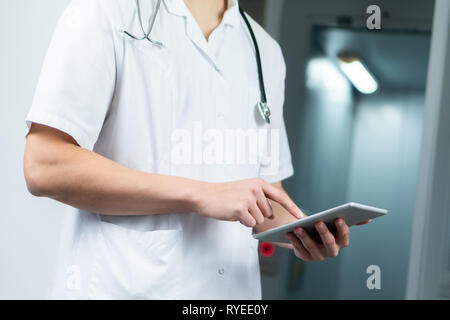 Bright close up of male doctor in uniform with stethoscope and using computer tablet in hospital. Modern medical concept Stock Photo