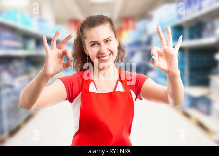 Female employee at hypermarket or supermarket making okay gesture with fingers at both hands and friendly expression Stock Photo