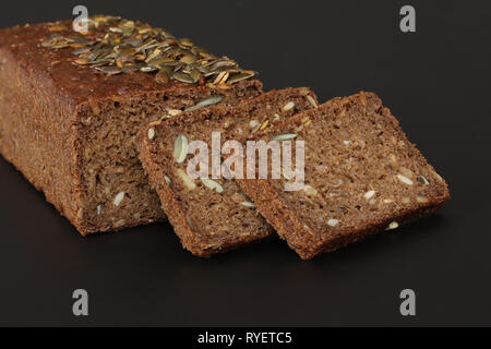 Home baked rye bread with sunflower  and pumpkin  seeds and cut off slices - close up on black background Stock Photo