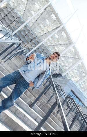 Outdoors Leisure. Mulatto guy standing on stairs with smartphone looking up motivated Stock Photo