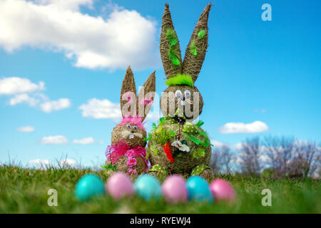 Straw Figure Bunnys With Colorful Easter Eggs green grassand blue sky Easter And Spring Background. blur Stock Photo
