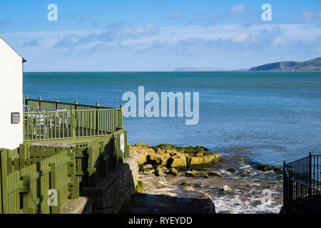 Bay Cafe and stream on rocky coast overlooking sea with Great Orme in distance. Benllech, Isle of Anglesey, North Wales, UK, Britain Stock Photo