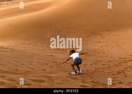 Young girl sandboarding in the desert - extreme desert activity in Dubai Stock Photo