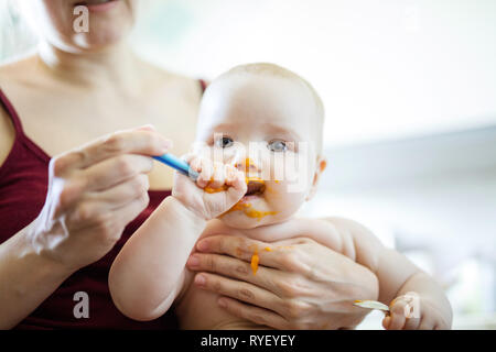 Mother feeding baby girl with spoon at home Stock Photo
