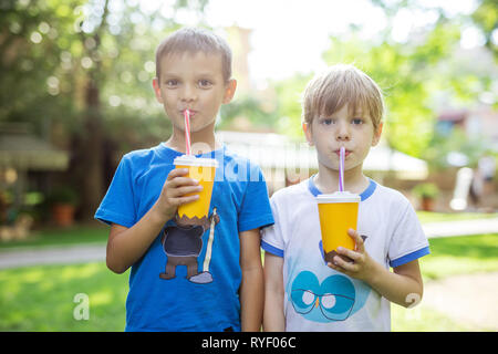 Two boys drinking cocoa from paper cups with straws in summer park Stock Photo