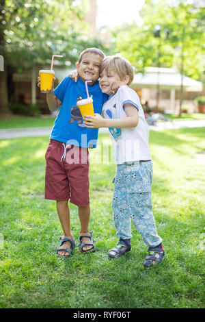 Two boys hugging one another or fighting jokingly while drinking cocoa from paper cups in park Stock Photo