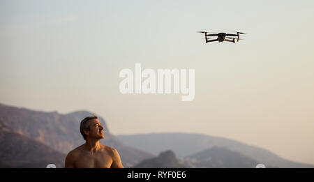 Caucasian man operating drone by remote control at sea shore at sunset Stock Photo