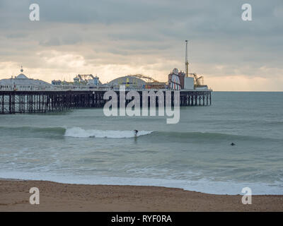 Surfers braving December cold sea by Brighton Pier on overcast winter day. Stock Photo