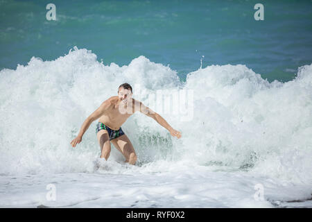 Young man enjoying high waves in rough sea, looking at camera and smiling Stock Photo