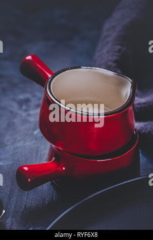 Vertical photo with two cups. Cups or small bowls have saturated red color, black edge and white inner side. Cups are stacked and placed on dark woode Stock Photo