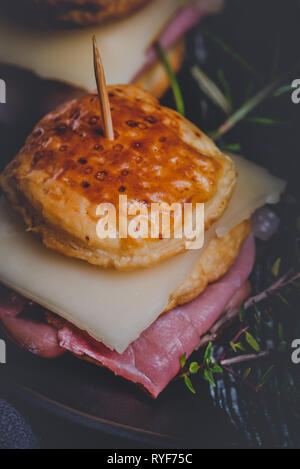 Vertical photo with two sandwiches. Sandwiches are from puff pastry dough squares stuffed by cheese and dried ham. Food is placed on black plate with  Stock Photo