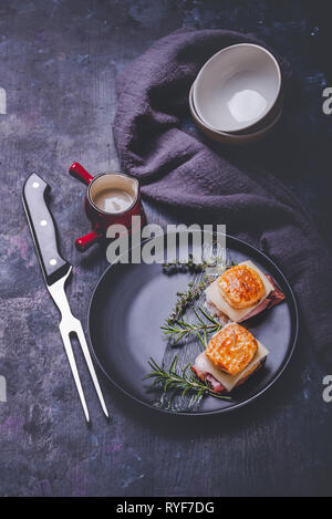 Vertical photo with two sandwiches. Sandwiches are from puff pastry dough squares stuffed by cheese and dried ham. Food is placed on black plate with  Stock Photo