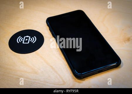 Smartphone charging on a table with a wireless charging pad. Wireless charging in common spaces like airports, cafes and stations concept Stock Photo