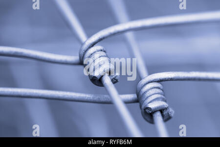 Fixed connection detail. Metallic wire fence. Artistic close-up of steel mesh in blue white tone. Abstract blurry background. Cohesion or safety idea. Stock Photo