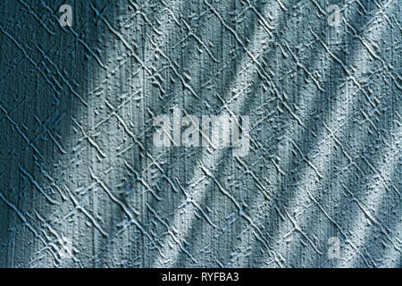 Pleasing texture detail of scratched stucco plaster. Interior close-up. Blue embossed wall lit by sunlight. Playful diagonal shadows. Retro background. Stock Photo