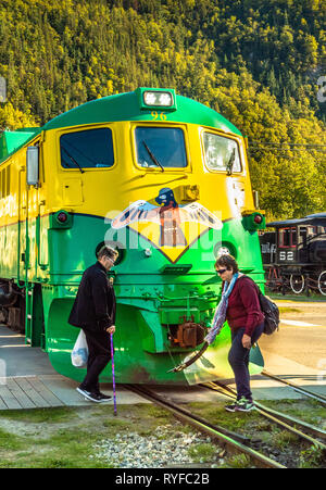 September 15, 2018 - Skagway, AK: Two female senior tourists crossing in front of Diesel-electric locomotive Engine 96 of the historic White Pass and  Stock Photo