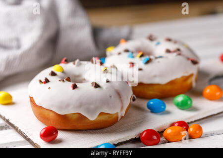 Cookery, baking and food concept - closeup. Two donuts in white glaze with color chocolate dragee on a decorative board on a dark background. Appetizi Stock Photo