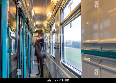 Motion blurred figure of conductor in the wagon of express train. The interior of moving train with long corridor and doors and windows. Stock Photo