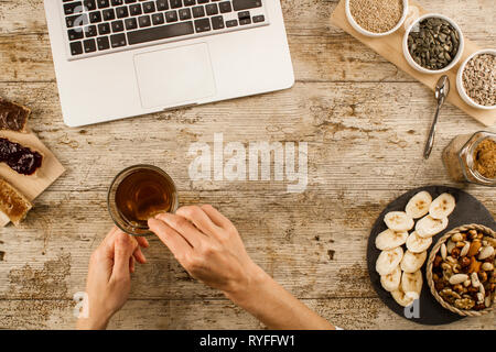 The habits of modern times: a woman shot from above on a wooden table, makes a healthy and vegan breakfast, but in front of the open laptop Stock Photo