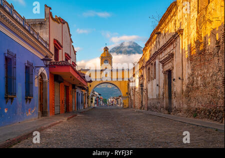 Cityscape of Antigua at sunrise with colonial style architecture and the yellow Santa Catalina arch with the Agua volcano in the background, Guatemala. Stock Photo