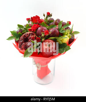 Beautiful bouquet consisting of pomegranate, apples, plums and scarlet roses standing in a vase on a wooden table Stock Photo