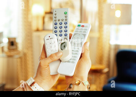 Closeup on remote controls in hands of modern woman in the living room. Stock Photo