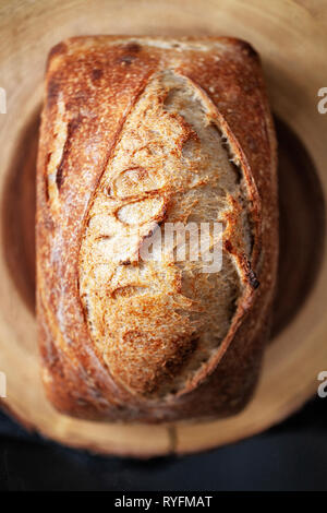 rectangle loaf of freshly baked homemade artisan sourdough bread on a round wood plank - image Stock Photo
