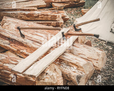 Construction site. Firewood with axes on a nature. Many logs wooden plank and three axes outdoor. Construction of a wooden bark. Stock Photo