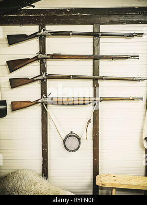 Old service rifles of British military with powder flask hanging on wooden wall. The fowling piece on a white wall Stock Photo