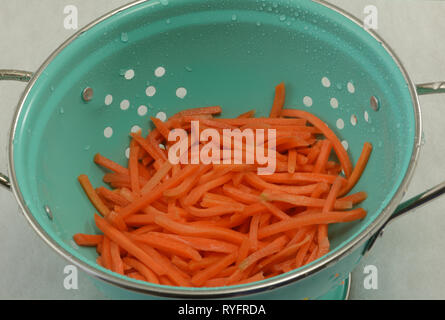 Rinsing and drying precut raw matchstick carrots in blue colander on white background Stock Photo