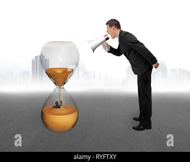 Boss using megaphone yelling at employee flooded in hourglass with city skyscraper and concrete floor background Stock Photo