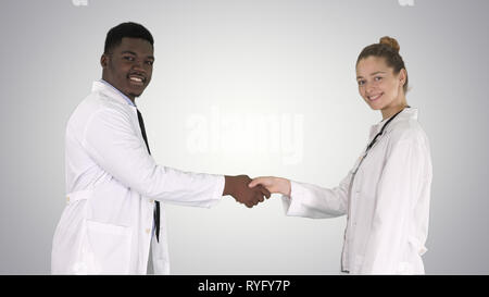 Doctors shaking hands and posing to camera on gradient background. Stock Photo