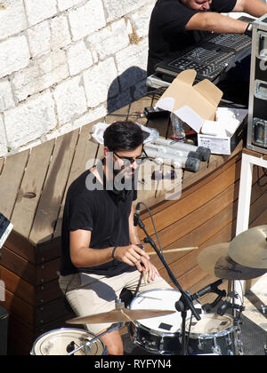 Greek drummer rehearsing in the sunshine before gig at a exclusive yacht club in Corfu, Kerkyra, Greece Stock Photo