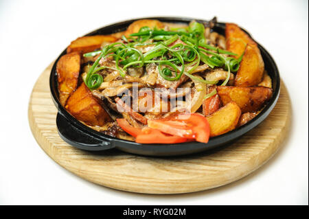 Fried potatoes with mushrooms, onions and bacon. This dish is cooked in a pan. Served on a wooden board. Stock Photo