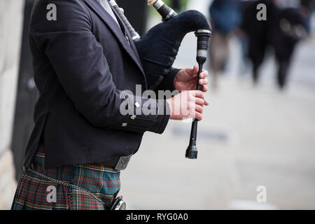 Scottish bagpiper dressed in traditional dress performing on the street Stock Photo