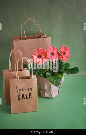 Coral gerbera daisy flowers and craft papper shopping bags on green paper background, Springtime sale concept image with copy-space Stock Photo
