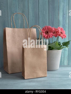 Coral gerbera daisy flowers and craft papper shopping bags on rustic background. Springtime sale concept image with copy-space Stock Photo