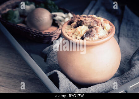 In a clay pot stewed beef with vegetables: potatoes, carrots, onions. Stock Photo