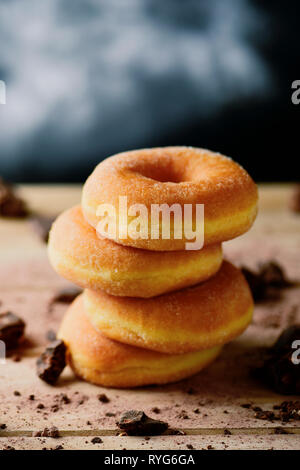 a stack of sugar glazed donuts on a rustic wooden table sprinkled with small pieces of chocolate Stock Photo