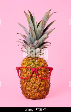 a pineapple wearing a pair of red lensless glasses on a pink background Stock Photo