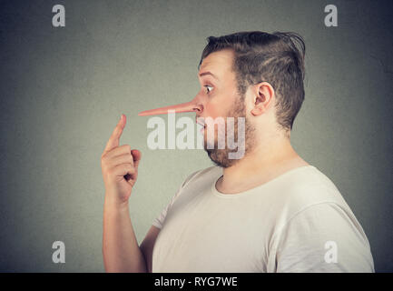Side profile of a shocked liar man with long nose feeling stunned isolated on gray wall background. Stock Photo