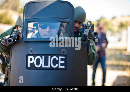 Military policeman aiming guns from behind a police riot shield. Stock Photo