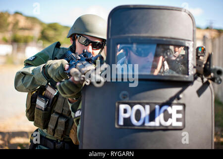 Military policeman aiming guns from behind a police riot shield. Stock Photo