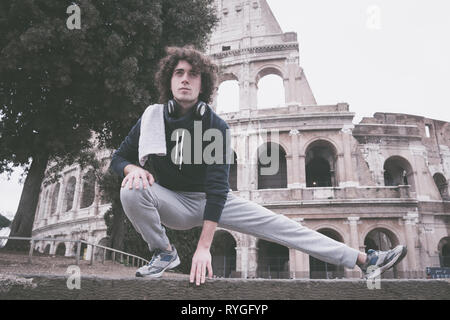 Handsome young sportsman stretching and warming-up for training in front of Colosseum in Rome Stock Photo